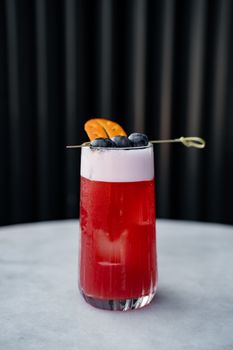 Refreshing red cocktail garnished with blueberries and citrus in a modern setting.