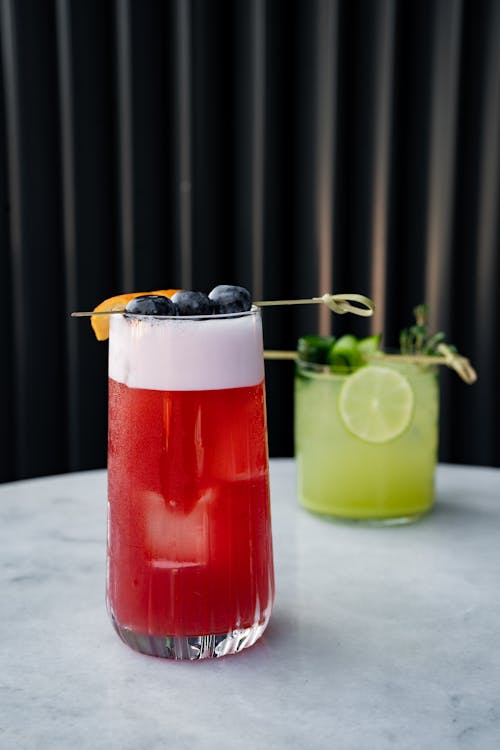 Two cocktails are sitting on a table with a lime and blueberry