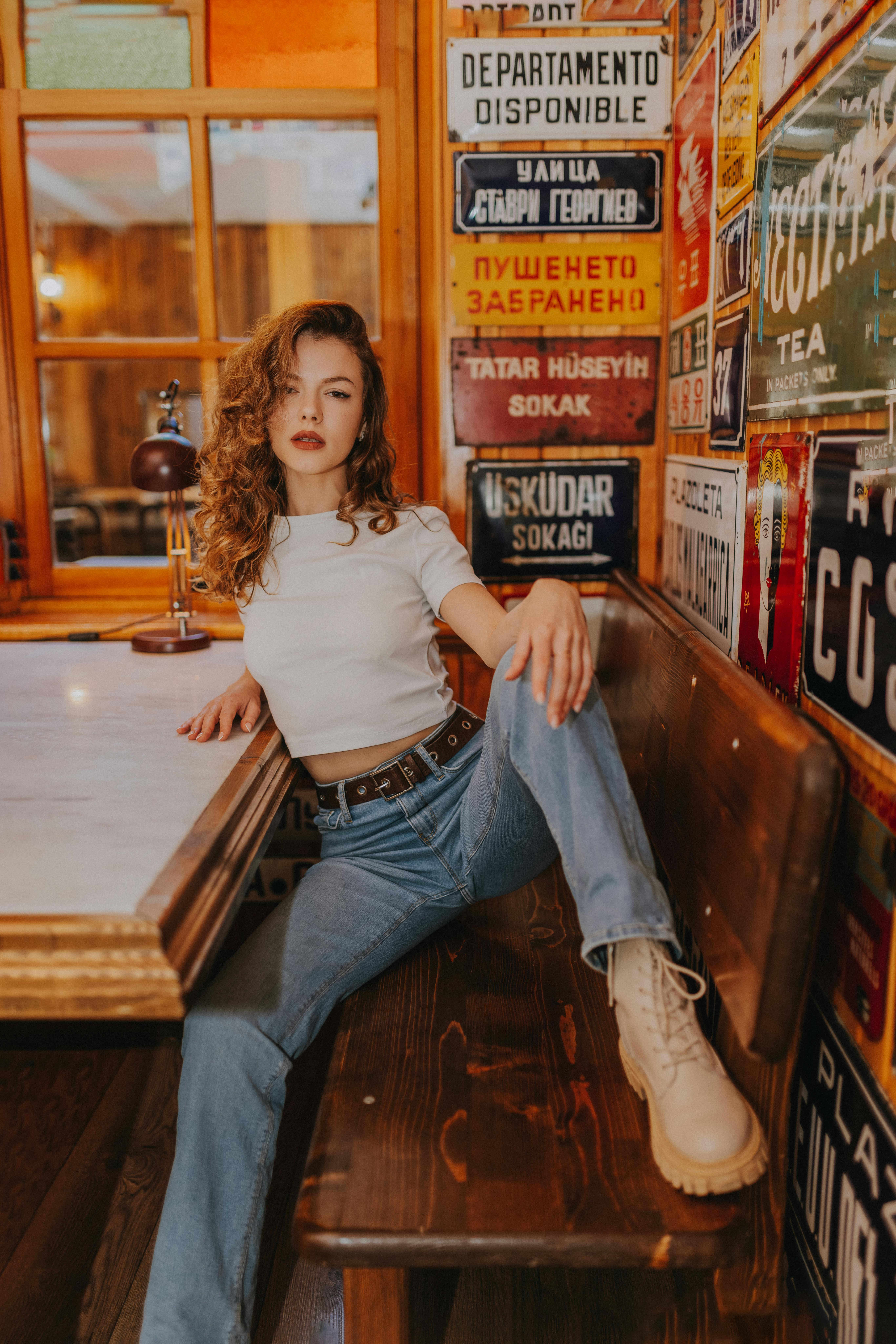 Trendy woman in casual attire posing confidently in a vintage-style cafe setting with colorful decor.