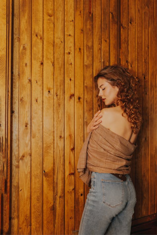 A woman in jeans leaning against a wooden wall