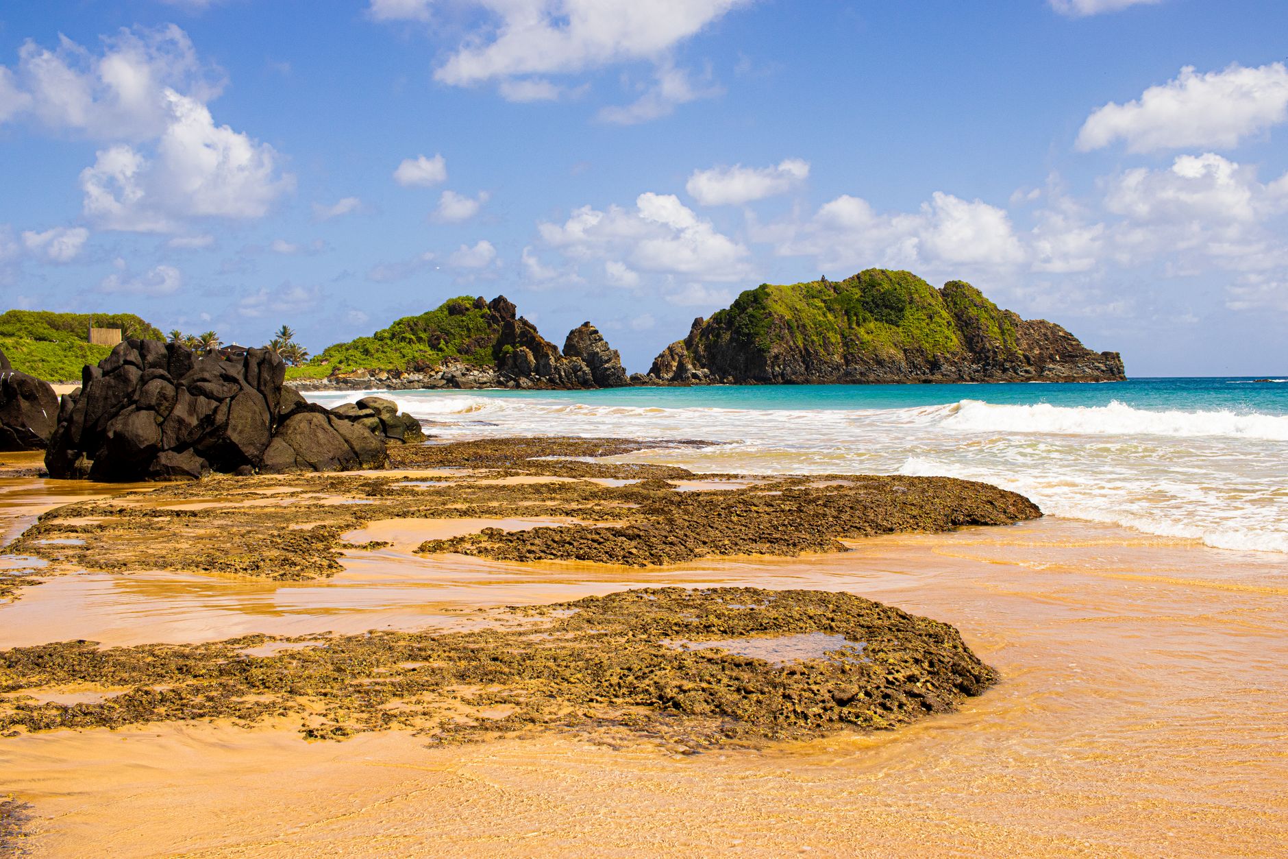 Explore a picturesque tropical beach with rocky shoreline, lush greenery, and clear blue skies.