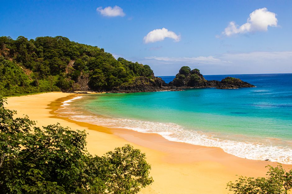Serene tropical beach with golden sands and crystal-clear waters surrounded by lush greenery on a sunny day.