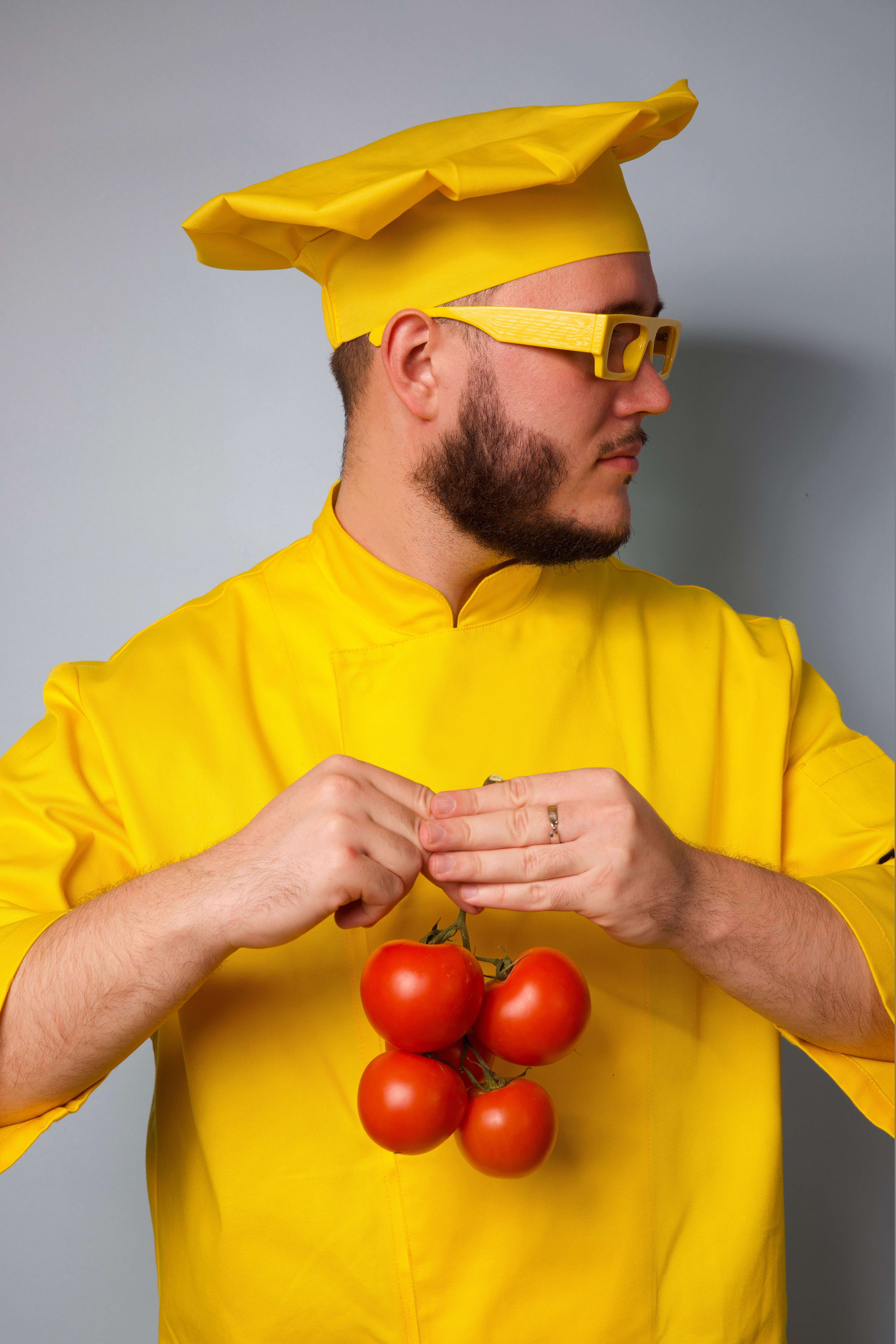 Vibrant portrait of a chef in yellow clothes holding tomatoes against a gray background.