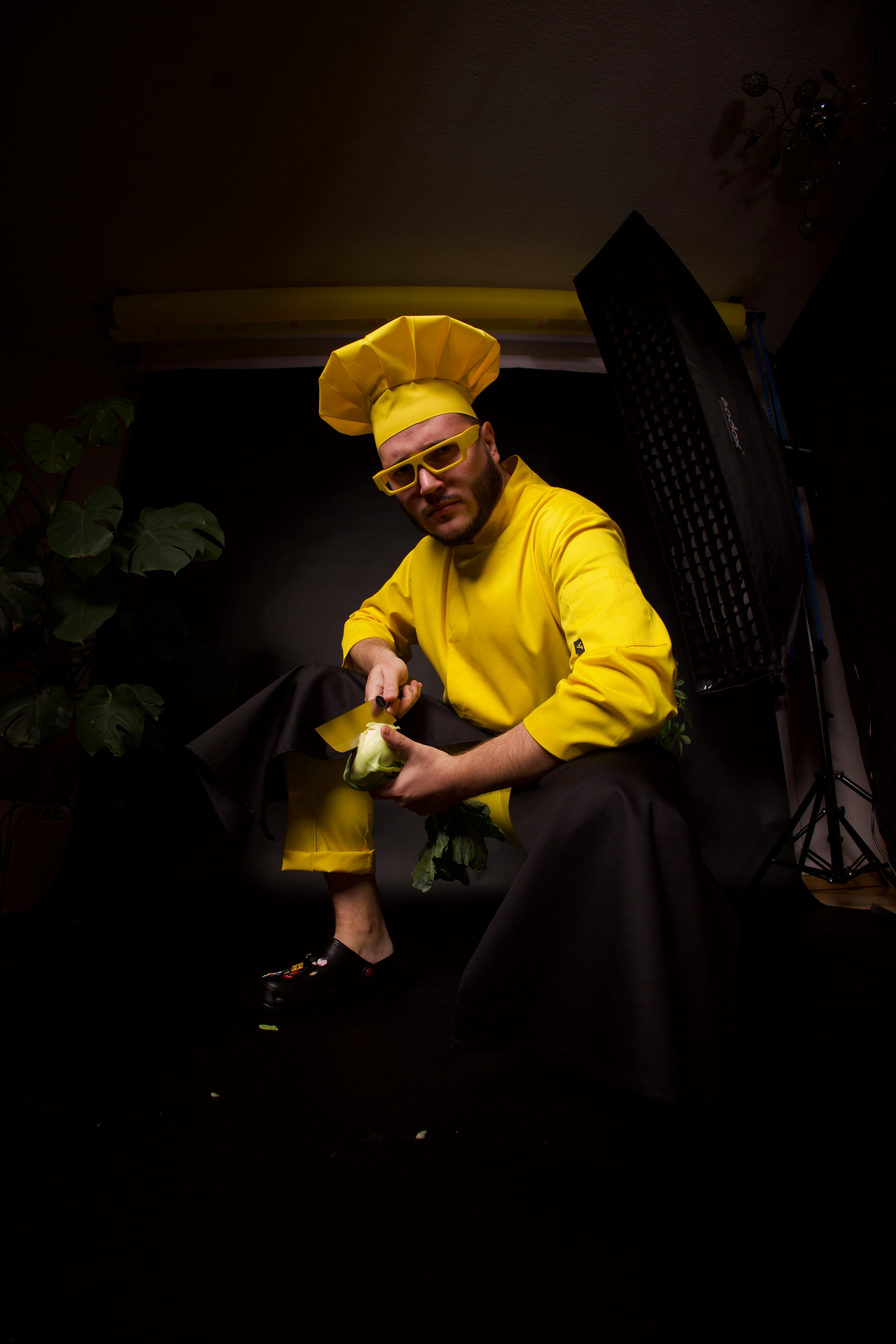 A chef in a vibrant yellow outfit posing with vegetables in a studio setting.