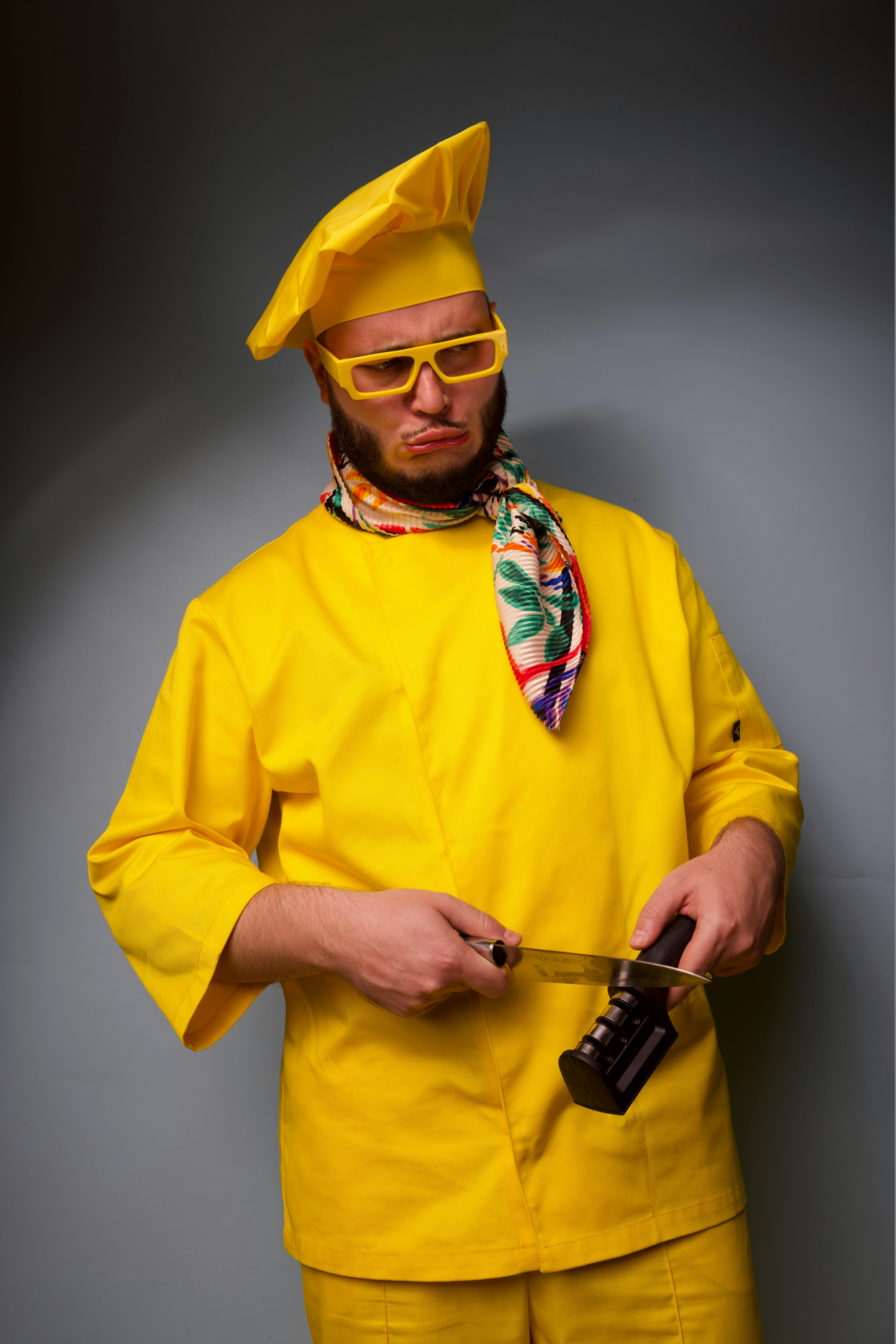 A playful chef wearing a bright yellow outfit and sharpening a knife with a humorous expression.