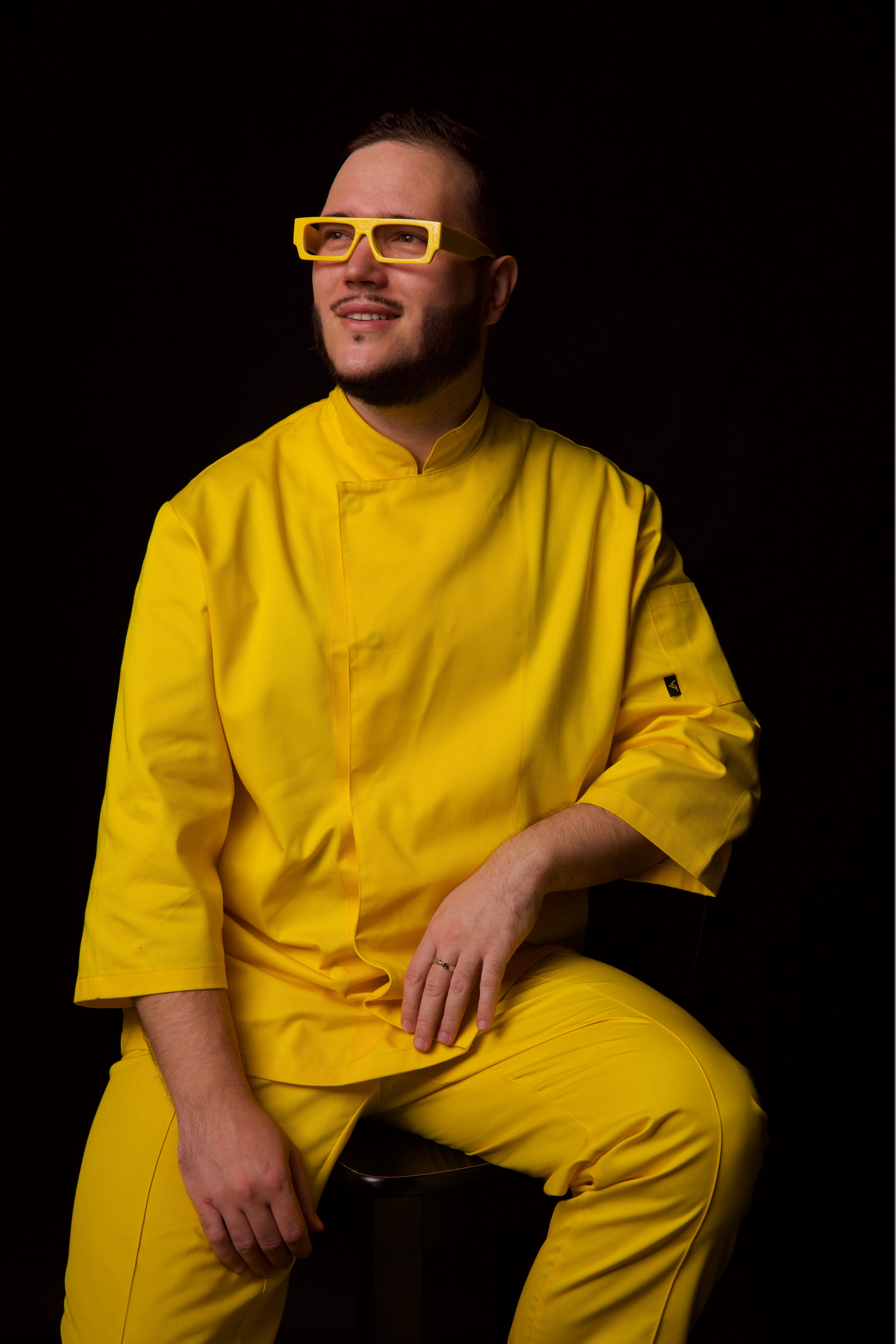 Man in stylish yellow outfit and glasses against black studio background.