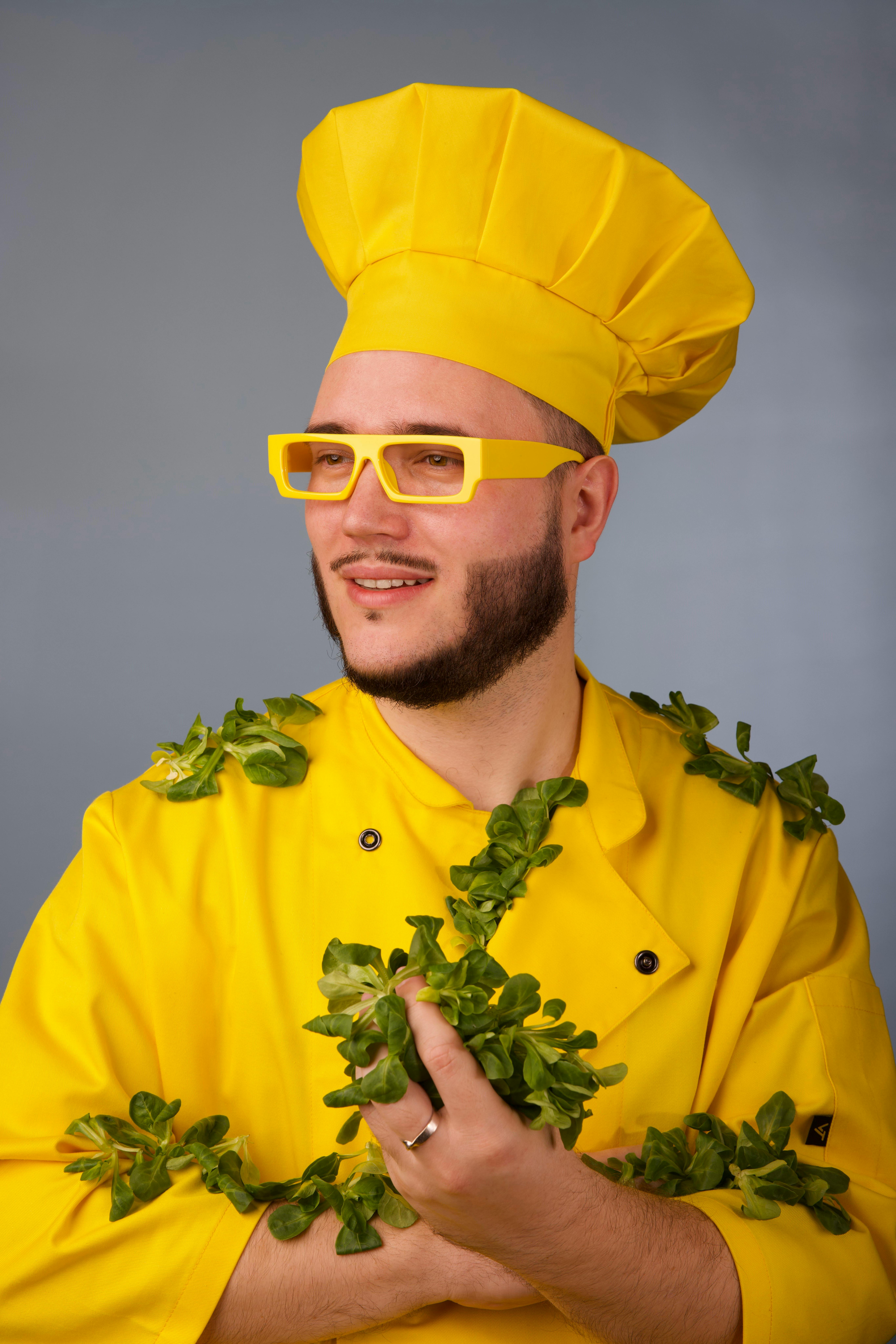Portrait of a chef in a yellow outfit adorned with fresh greens, exuding creativity and culinary flair.