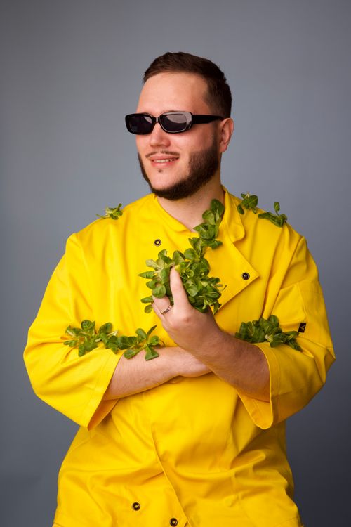 Free Fashionable man in sunglasses and yellow jacket holding greenery against gray background, smiling. Stock Photo