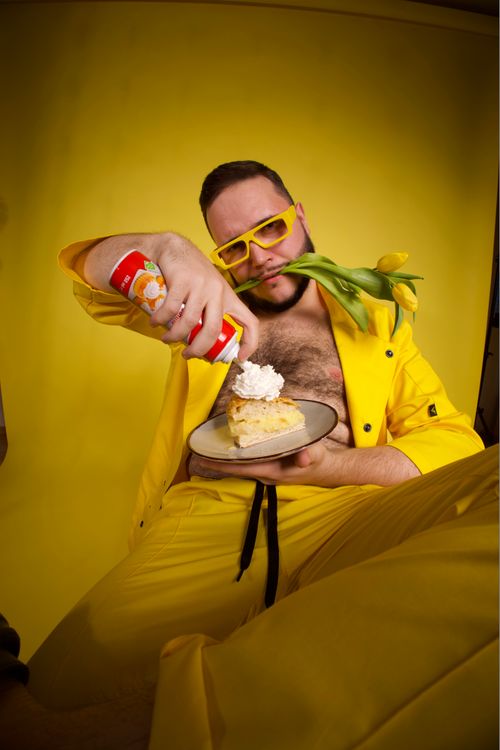 Free A man in vibrant yellow attire adds whipped cream to a cake slice in a colorful studio setting. Stock Photo