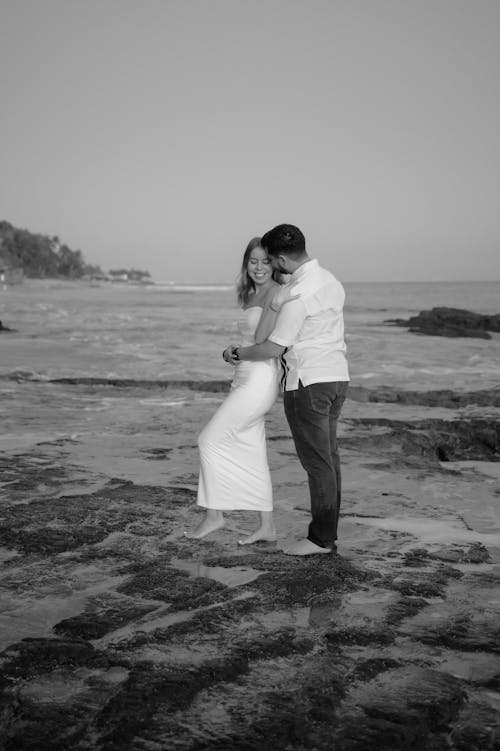 A couple standing on the beach in black and white
