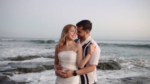 A bride and groom standing on the beach in front of the ocean