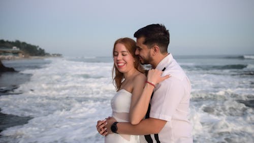 A bride and groom are standing on the beach