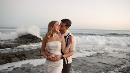 A bride and groom standing on the beach with waves crashing behind them