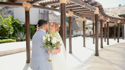 A bride and groom kiss under an arbor