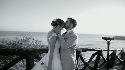 A bride and groom kiss in front of the ocean