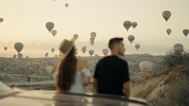 Couple watching hot air balloons at sunrise in Cappadocia, Türkiye, a popular travel destination.