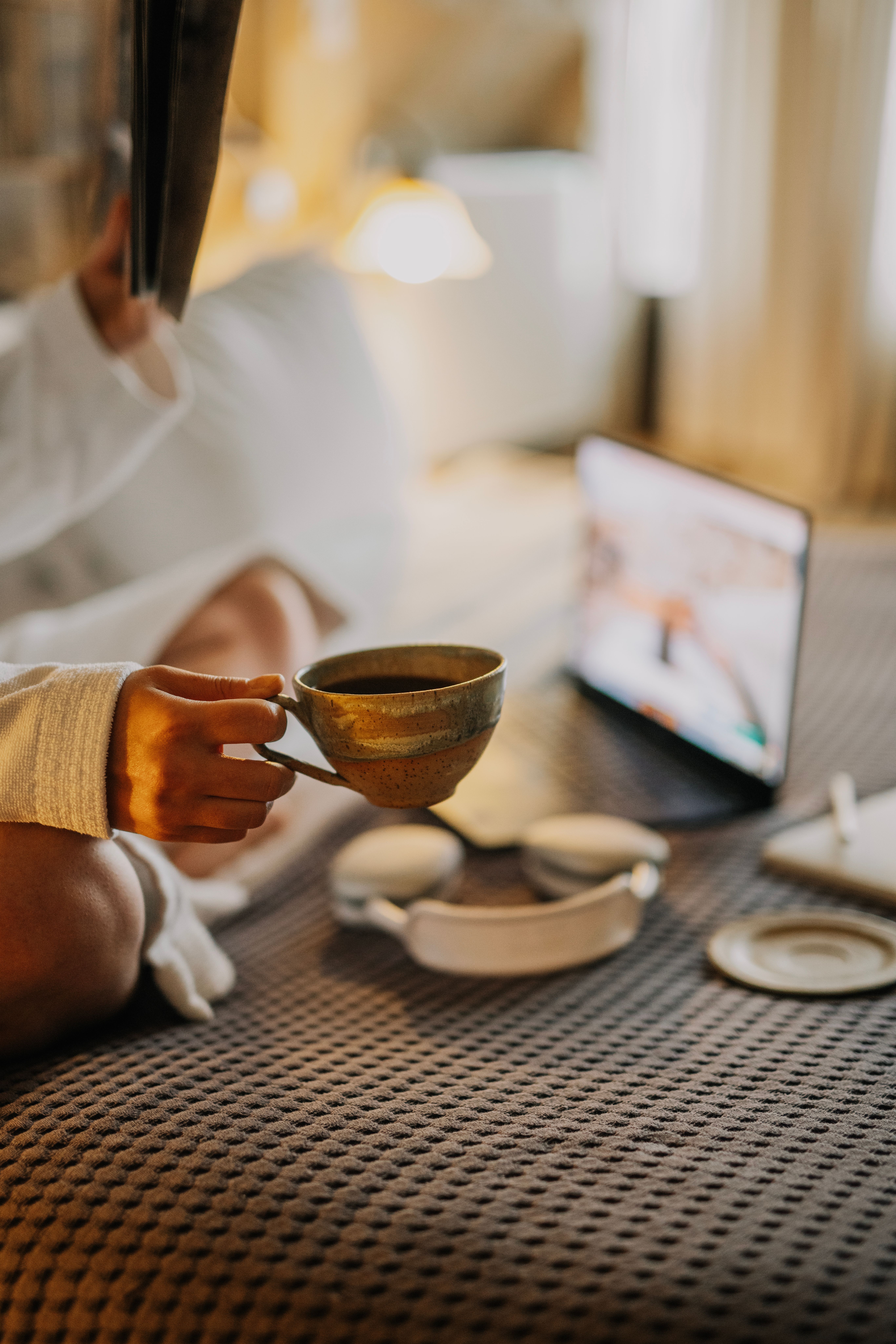 A woman enjoys coffee in bed while browsing on her laptop. Perfect for relaxation themes.
