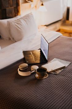 A cozy hotel room setup with coffee, laptop, and headphones on the bed, perfect for relaxation.