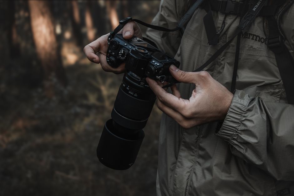 Close-up of a photographer holding a camera in a dimly lit forest environment.