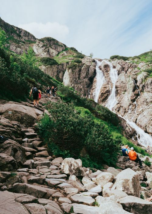 Free A breathtaking waterfall with hikers enjoying the serene mountain landscape in summer. Stock Photo