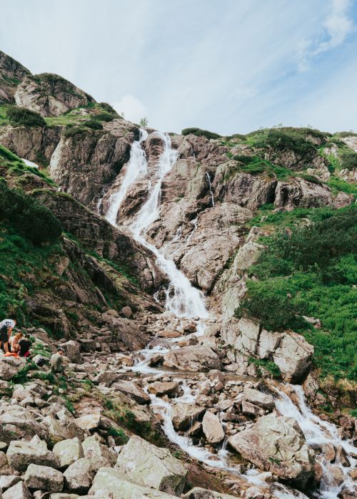 Free A breathtaking waterfall cascades down a rocky mountain amidst lush greenery, perfect for nature lovers. Stock Photo