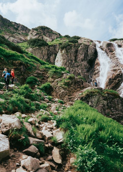 Free Group of hikers exploring a scenic waterfall in the Tatra Mountains during summer. Stock Photo