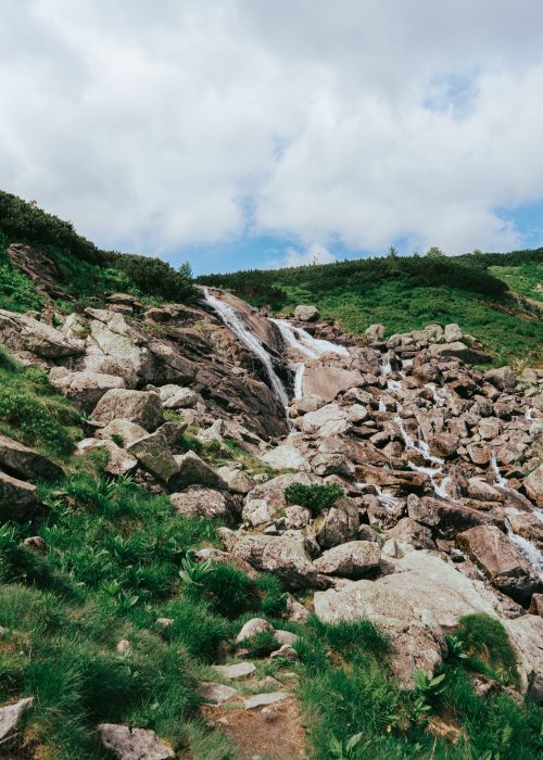 Free Breathtaking waterfall cascading over rocks in a lush, green mountainous landscape. Stock Photo