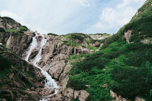 Free Stunning waterfall cascading down rocky cliffs amid lush greenery under a clear summer sky. Stock Photo