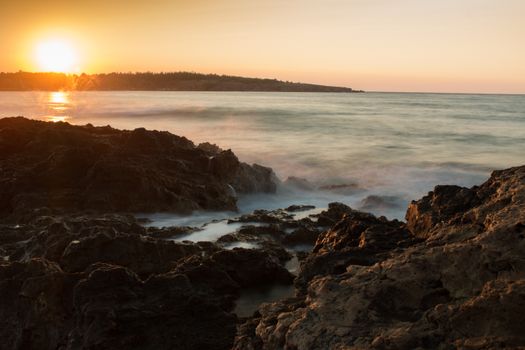 Beautiful sunset over a rocky coastline with calm waves and golden sky.