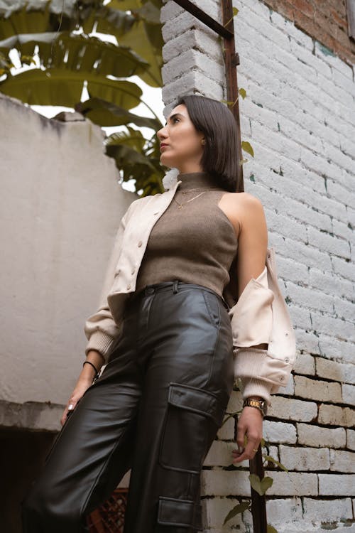 A woman in leather pants leaning against a brick wall