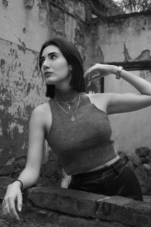 A woman in a black top and jeans leaning against a wall