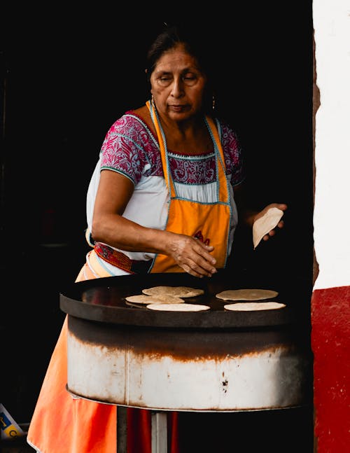 A woman making tortillas in a small kitchen