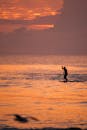 宁静的海水上充满活力的日落中，一个人在桨板冲浪的剪影