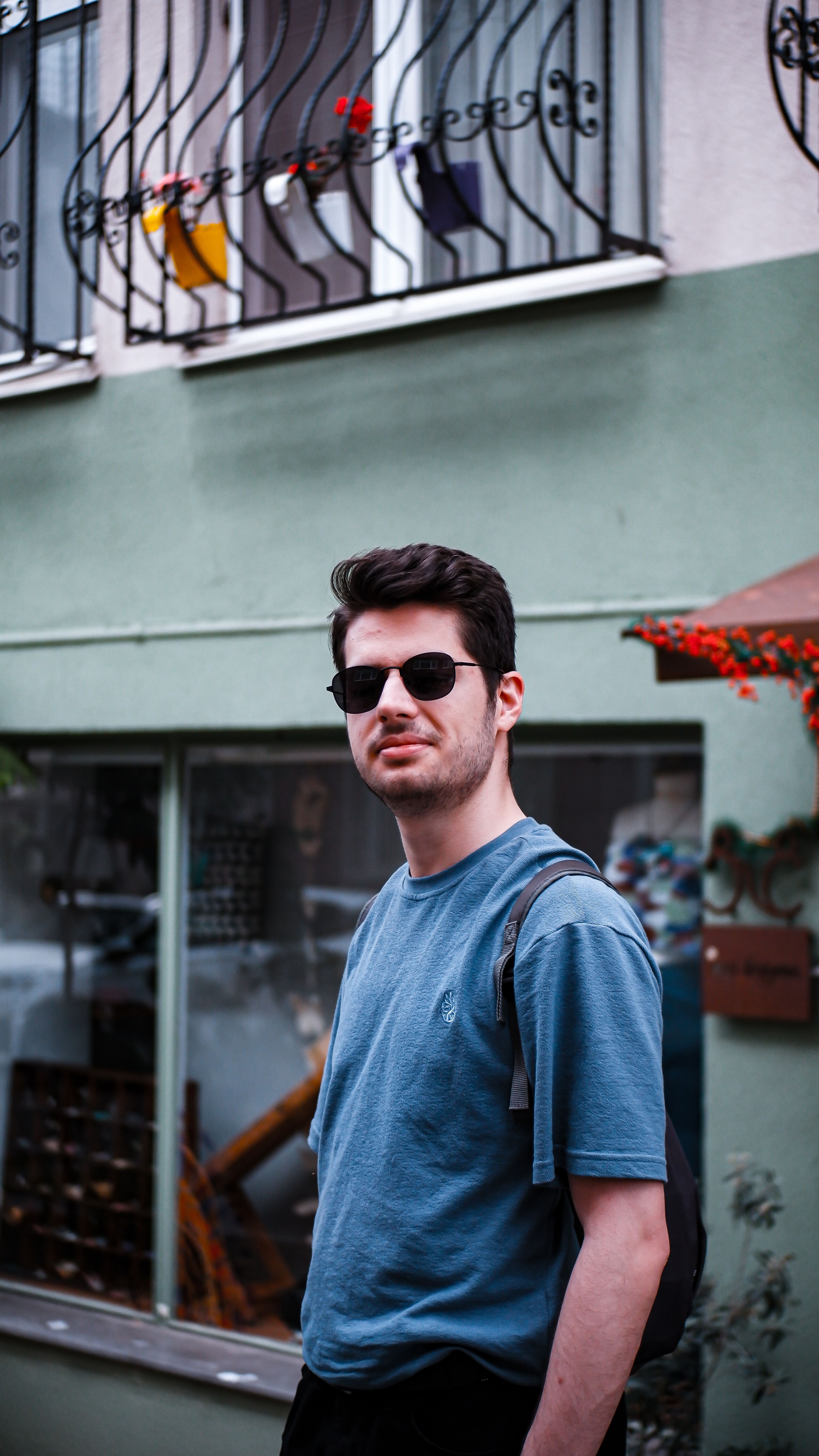 Man wearing sunglasses and t-shirt standing outdoors in a city residential area.