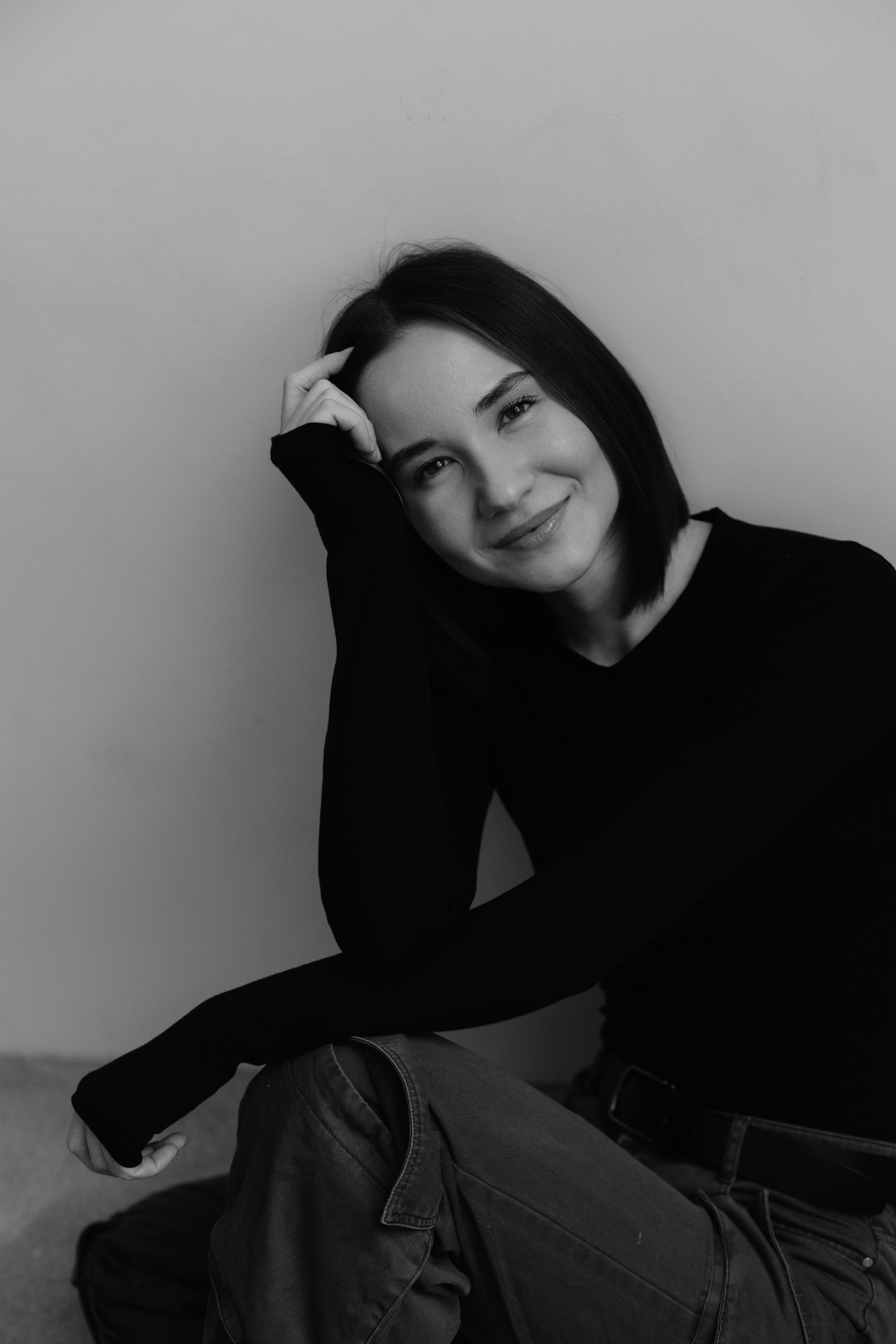 A minimalist black and white portrait of a young woman smiling in a studio setting.