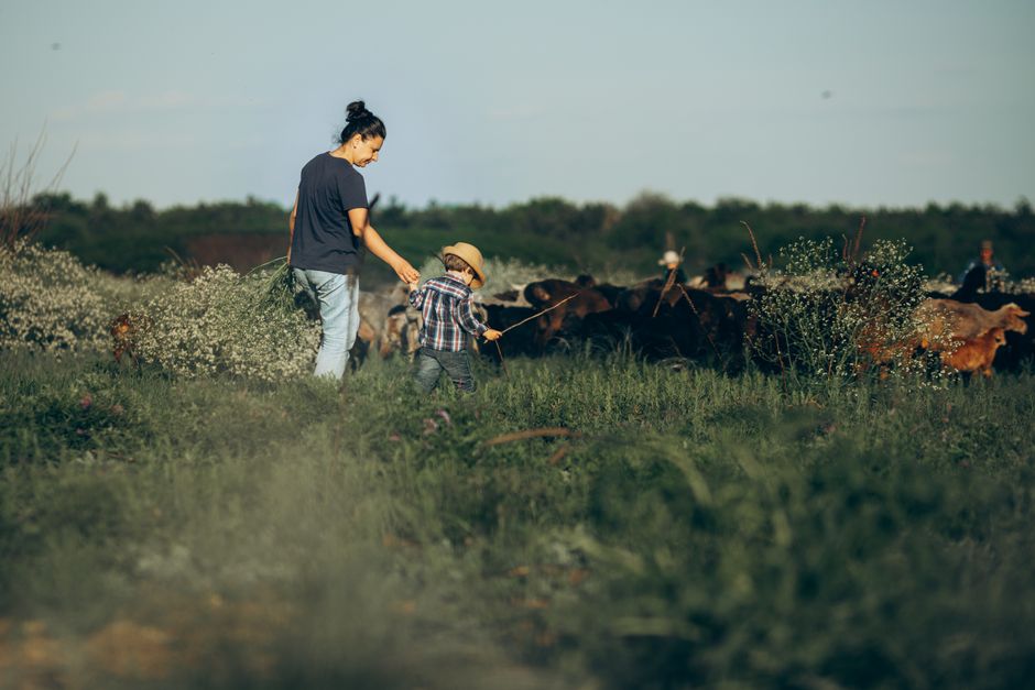 Una madre y su hijo pastoreando cabras juntos en un entorno pintoresco de pradera, capturando la vida rural.