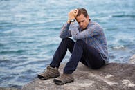 一个穿着休闲服的男人坐在海边的岩石上，神情显得很周到