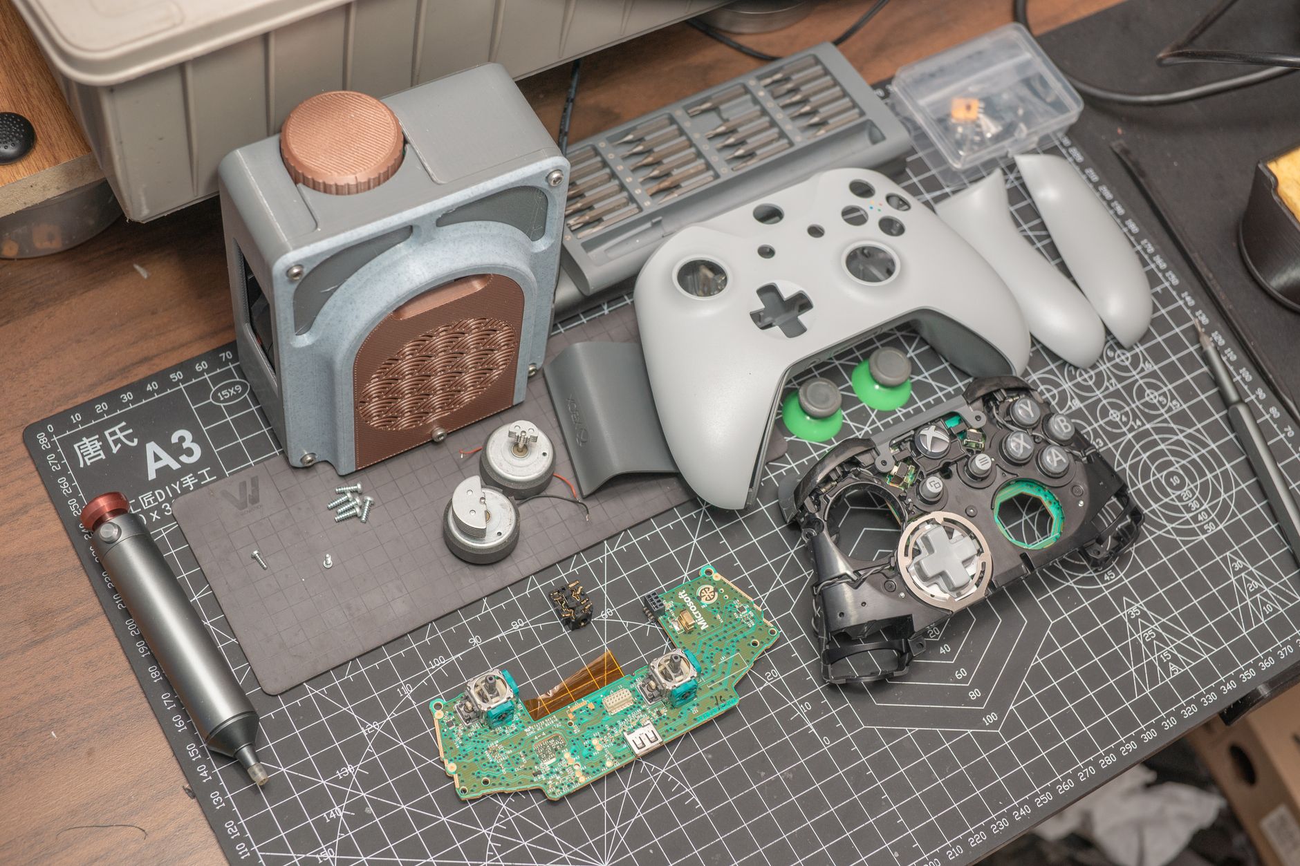 A disassembled video game controller and components set on a desk mat, illustrating electronics repair.