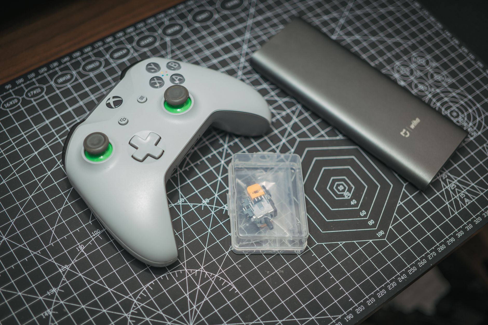 A flat lay of a wireless Xbox controller, power bank, and tech accessories on a patterned desk mat.
