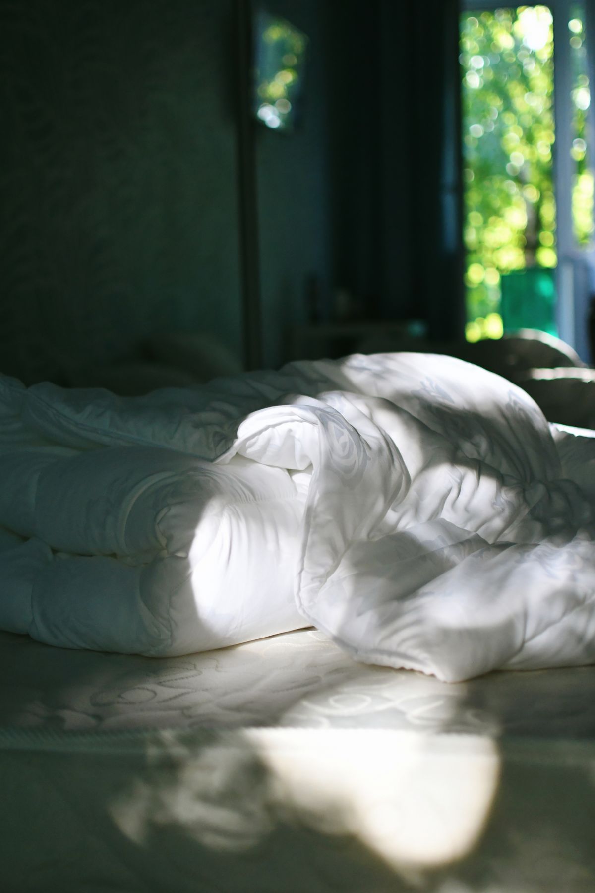 White bedding on a bed with an open window and green garden light, suggesting cool fresh air.