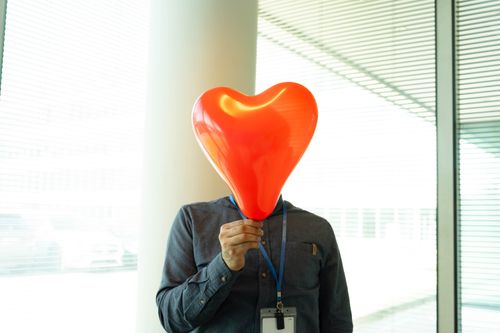 Free Humorous concept of a man holding a heart-shaped balloon over his face in an office setting. Stock Photo