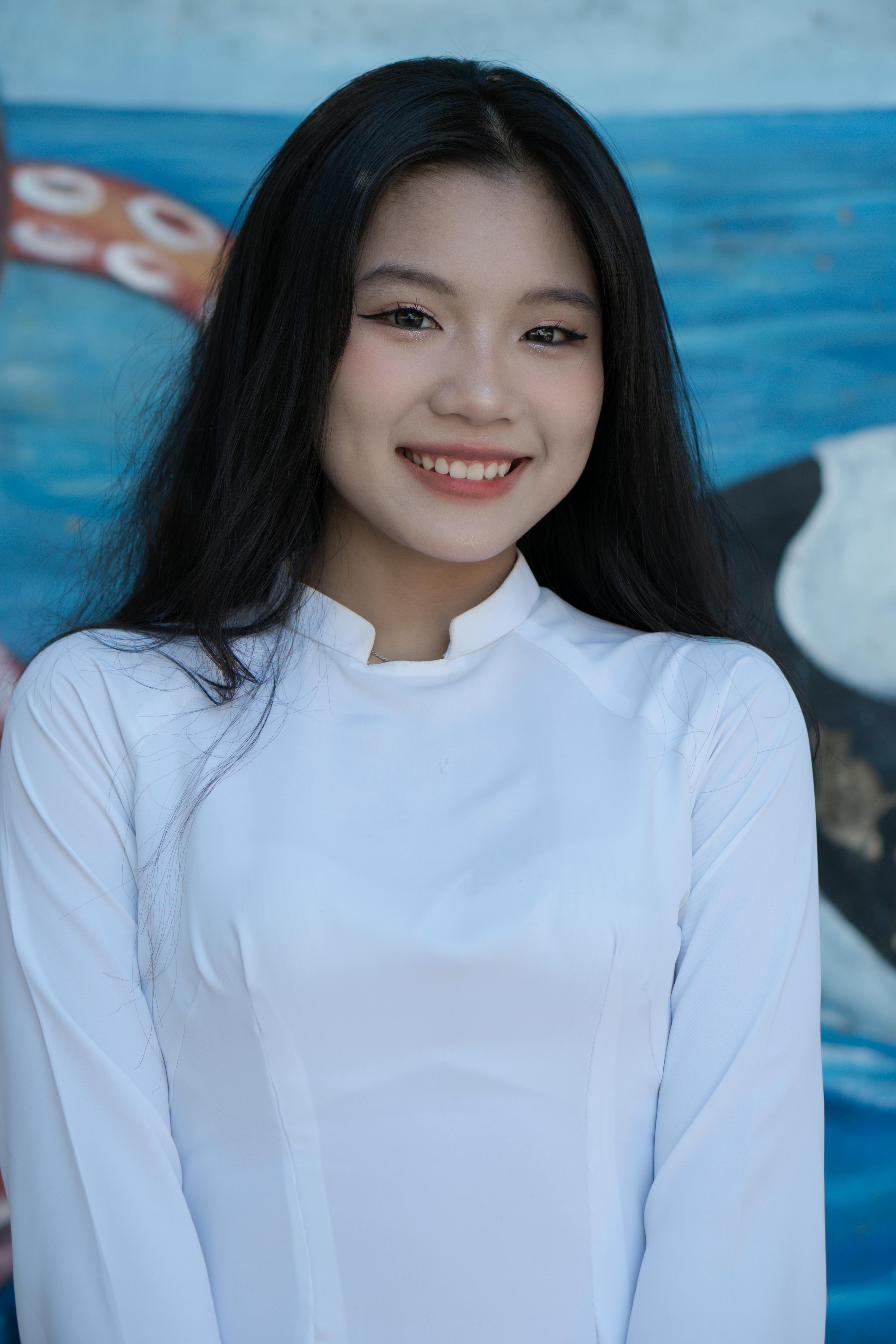 Close-up of a smiling Asian woman in a white tunic against a colorful background.