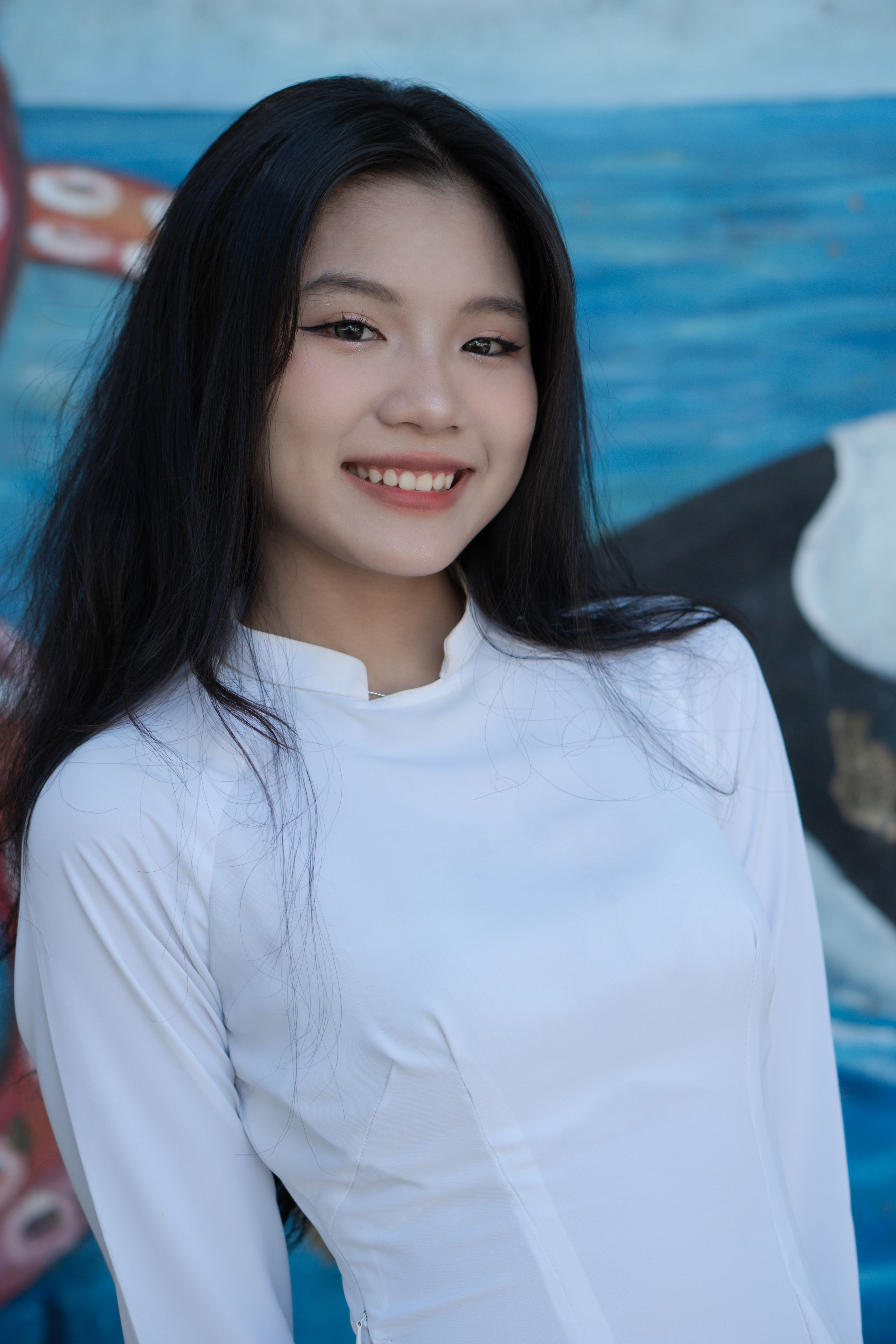 Portrait of a smiling woman in a white tunic against a colorful background, exuding elegance and joy.