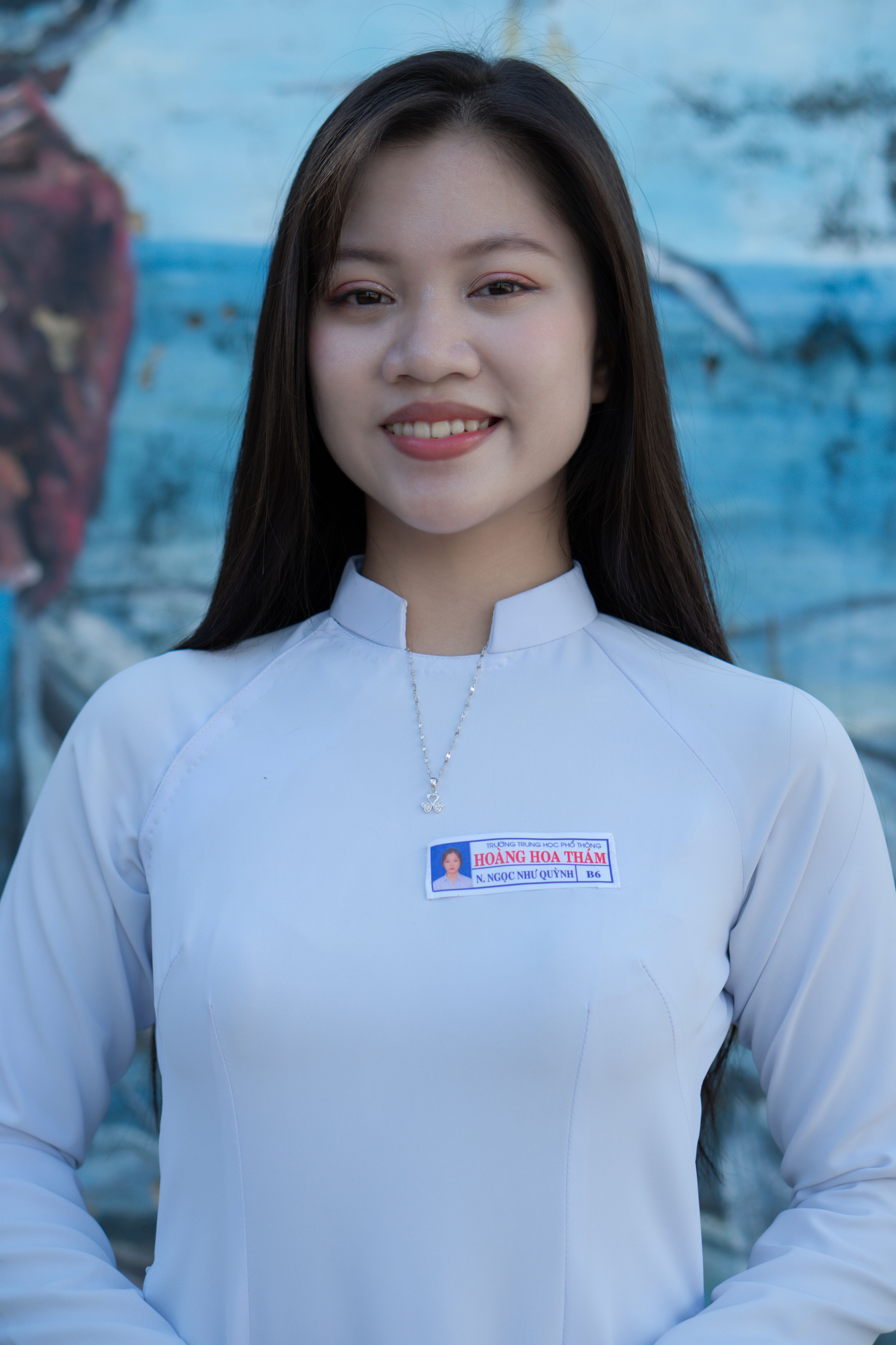 Elegant woman in a white tunic smiling confidently, outdoors portrait.