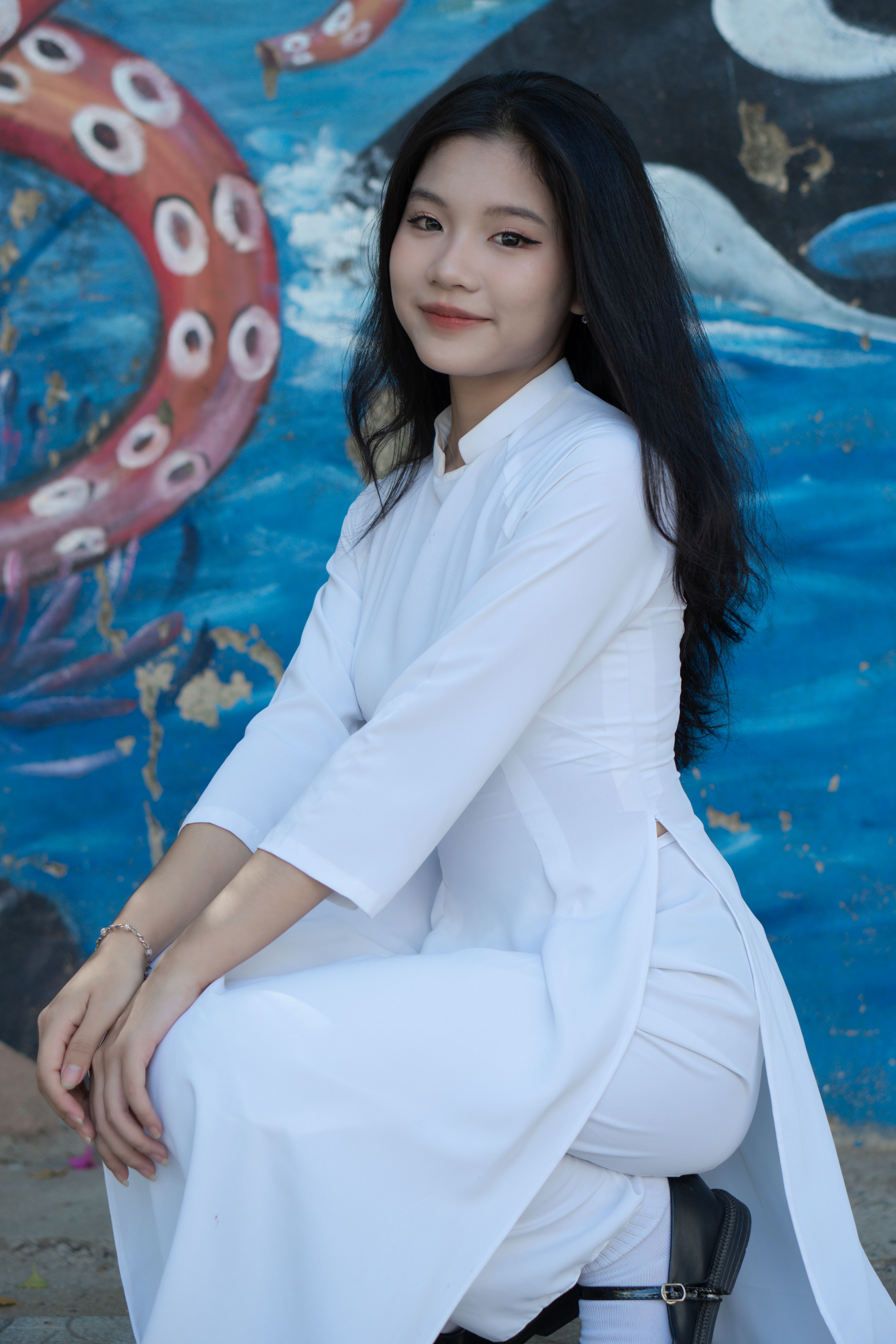 A young Asian woman in a white tunic poses confidently in an artistic, aquatic-themed setting.