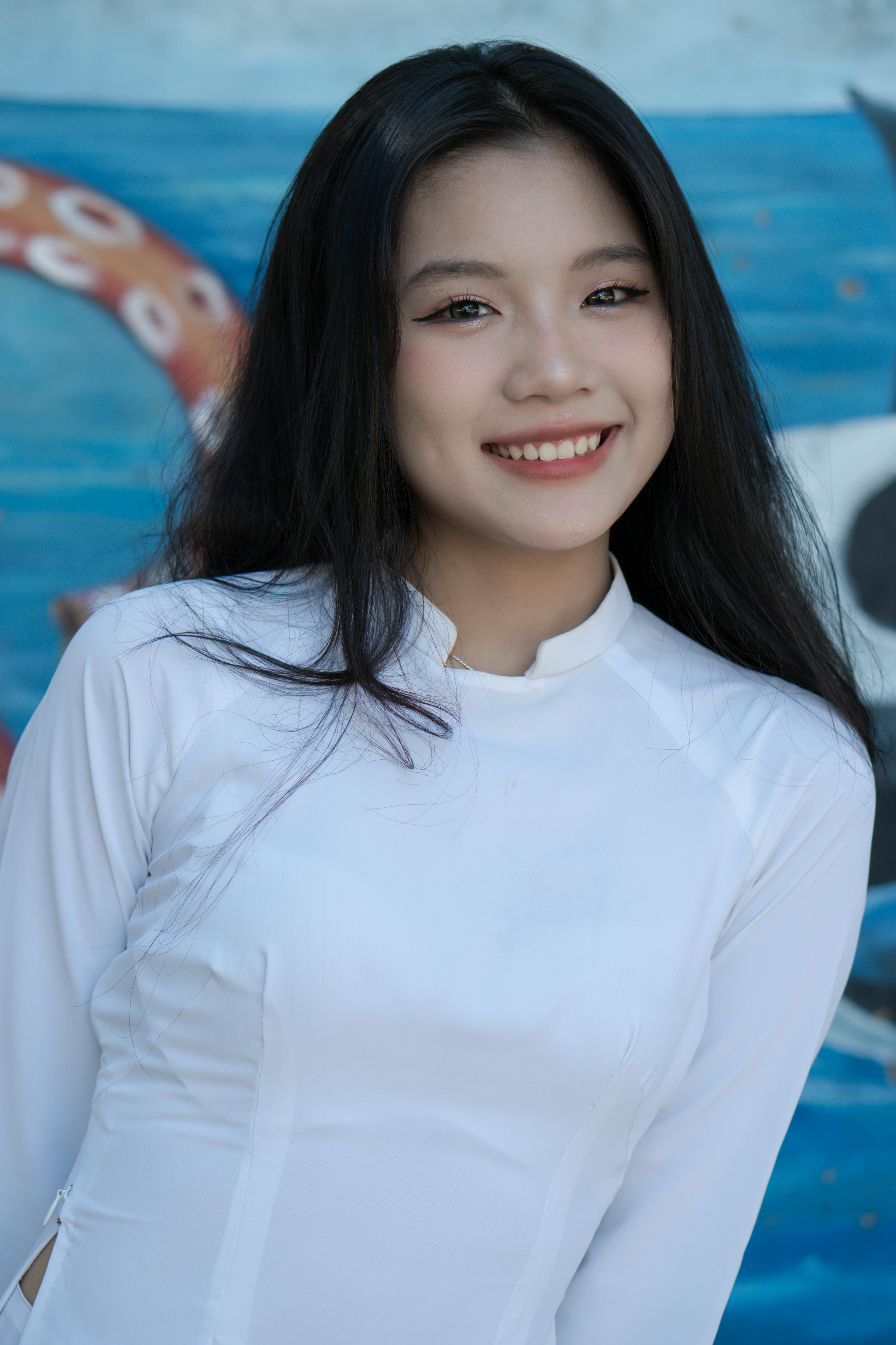 Portrait of a smiling woman in a white tunic with a vibrant blue mural behind her.