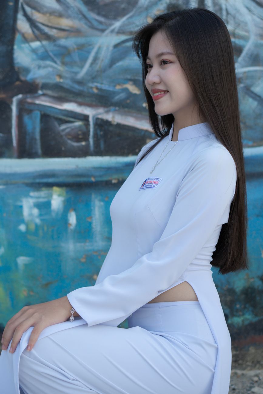Side profile of a smiling woman in traditional white attire against a mural background.