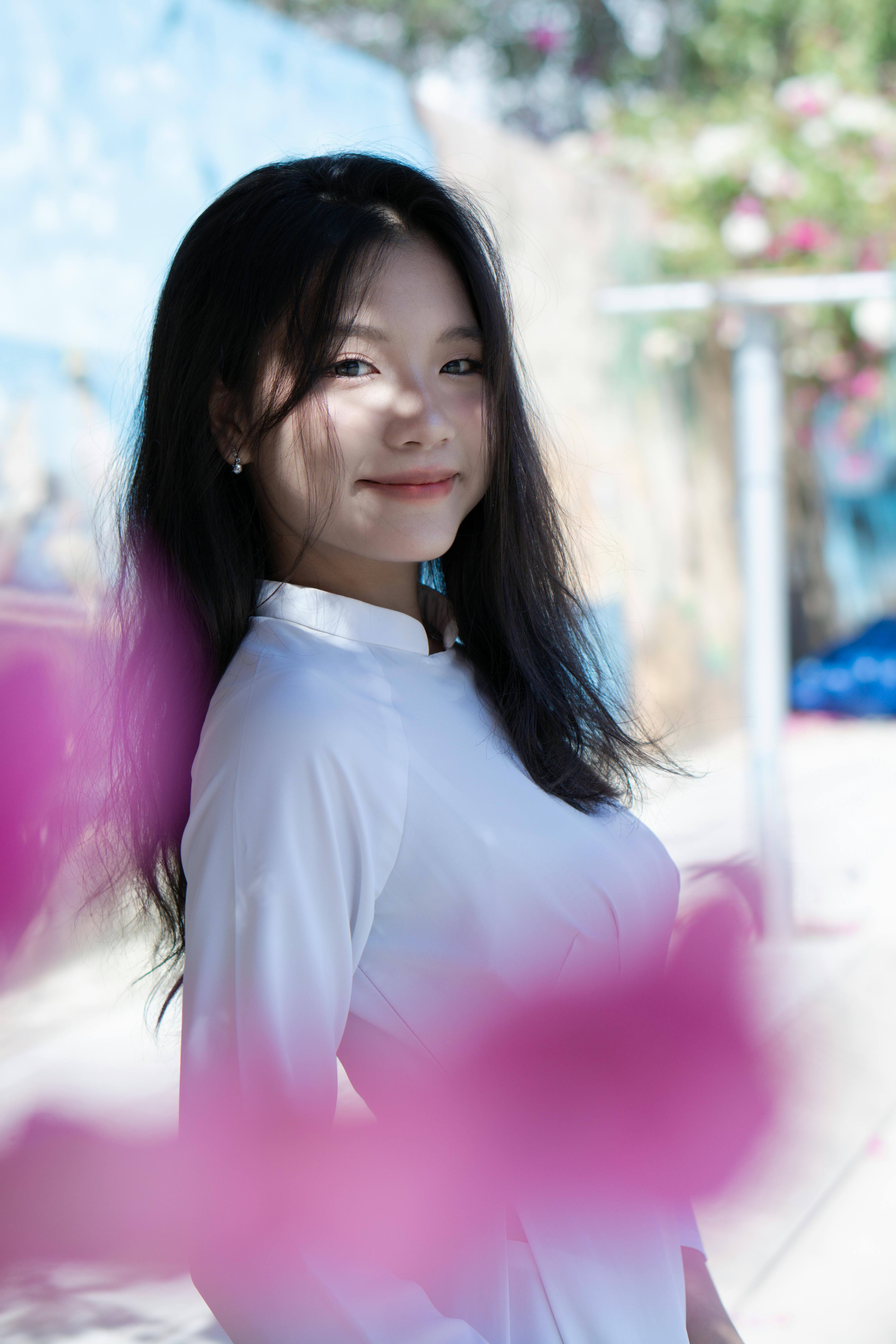 Elegant portrait of a smiling woman in white traditional clothing, surrounded by flowers.