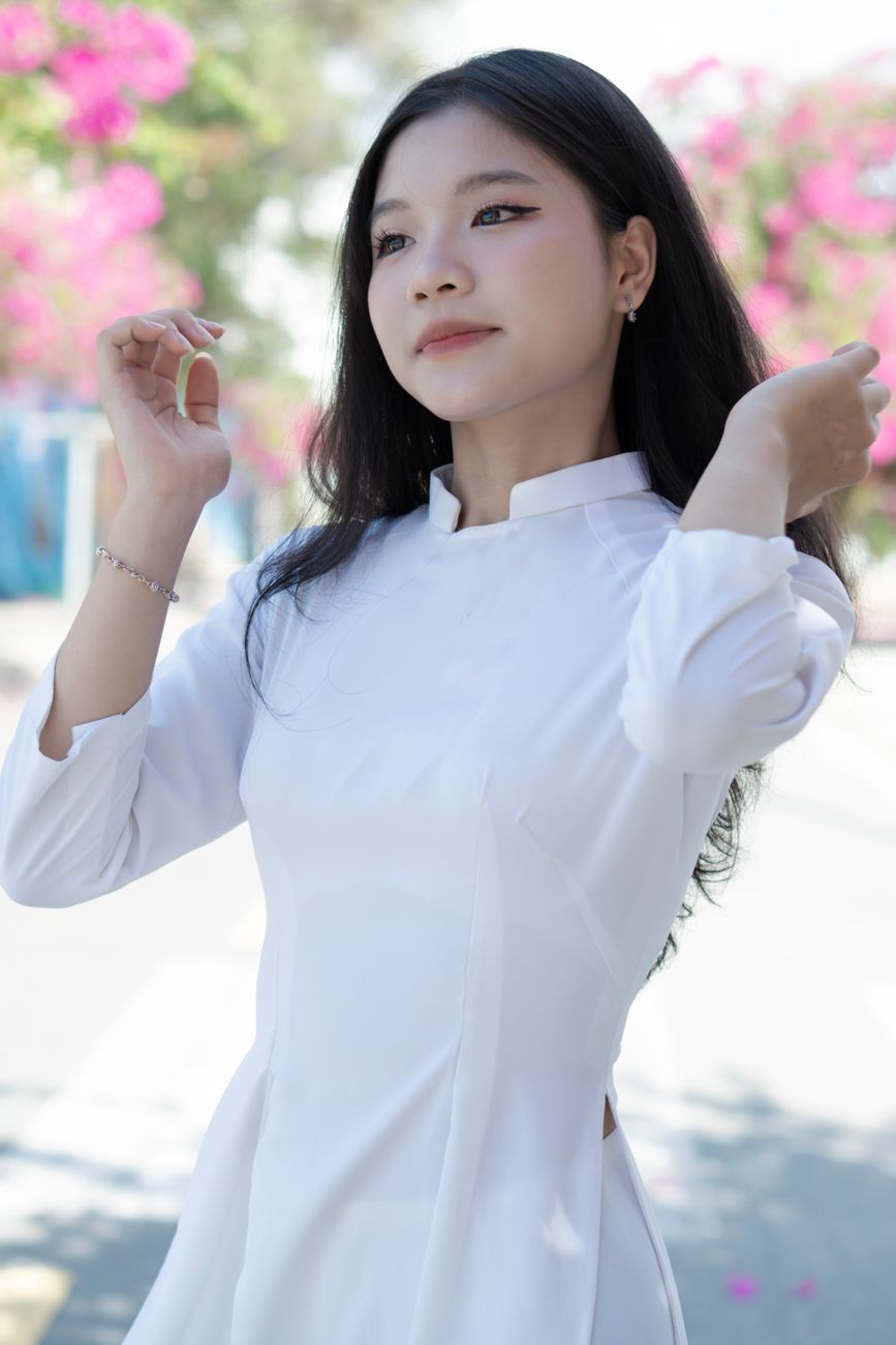 Asian woman in traditional white dress posing elegantly outdoors.