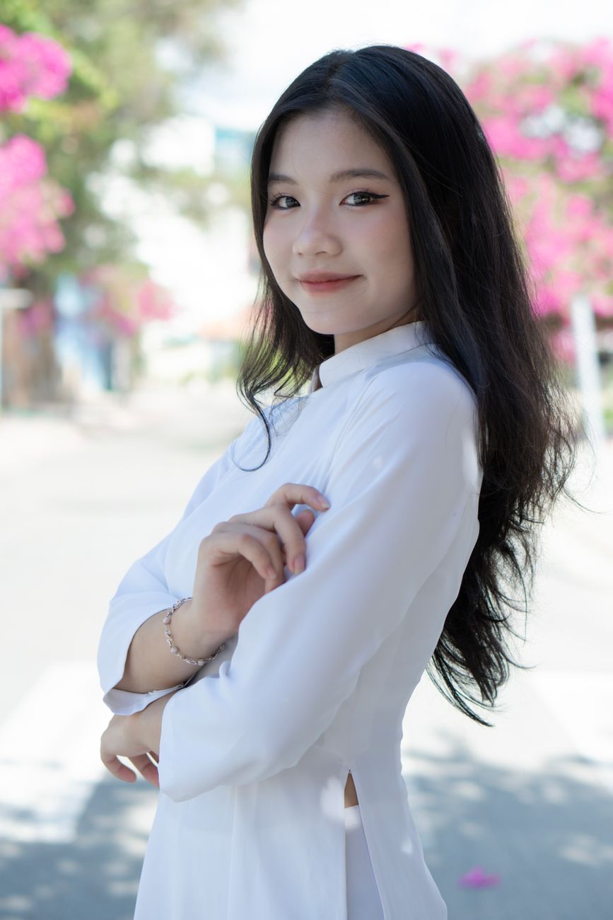 Portrait of a smiling woman in a white Ao Dai, showcasing elegance and traditional fashion outdoors.